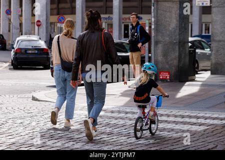 Ein junges Paar und ihre kleine Tochter, von hinten gesehen, fahren auf dem Fahrrad, während sie die Fußgängerüberquerung überqueren Stockfoto