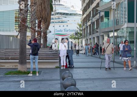 Savona. Italia - 07. Dezember 2024: Touristen wandern und fotografieren in der Nähe des Kreuzfahrtschiffs Costa Fortuna, das im Hafen von Savona, Italien, mit m Stockfoto