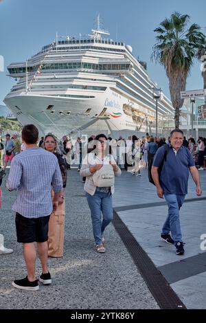 Savona. Italia - 07. Dezember 2024: Menschen genießen einen sonnigen Tag im Hafen von Savona, Italien, mit dem Kreuzfahrtschiff Costa Fortuna im Hintergrund und Stockfoto