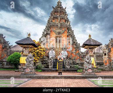 Junge weibliche Touristen in traditioneller balinesischer Kleidung beten mit ihren Händen zusammen vor einem Tempel in Bali, Indonesien, mit einem dramatischen Stockfoto