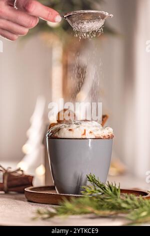 Koch streut Puderzucker auf köstliche heisse Weihnachtsschokolade mit verschwommenem festlichem Hintergrund Stockfoto