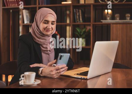 Eine glückliche muslimische Geschäftsfrau, die ein Telefon benutzt, während sie im Büro arbeitet. Stockfoto