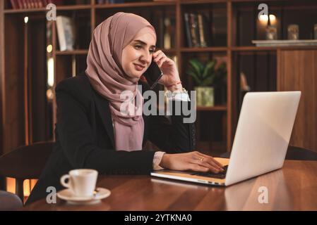 Eine glückliche muslimische Geschäftsfrau, die während ihrer Arbeit im Büro telefoniert. Stockfoto