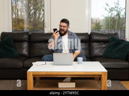 Wütender, gestresster Mann, der während seines Telefongesprächs mit einem Burnout-Gesichtsausdruck geschrien hat, während er im Heimbüro arbeitet. Stockfoto