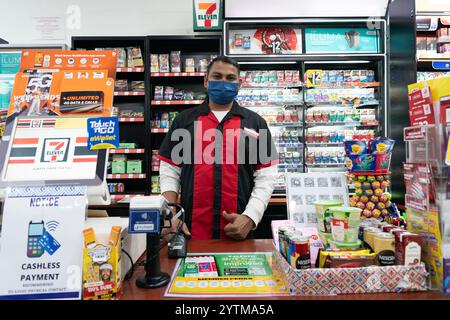 KUALA LUMPUR, MALAYSIA - 8. NOVEMBER 2023: Ein Kassierer posiert für ein Foto in einem 7-Eleven, einer globalen Lebensmittelhandelskette, die Snacks, Getränke und e anbietet Stockfoto