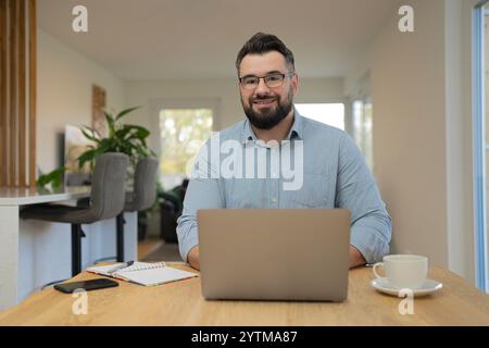 Ein glücklicher Mann, der einen Laptop benutzt, während er im Heimbüro arbeitet. Stockfoto