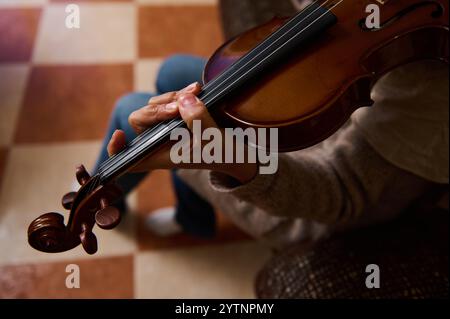 Ein detaillierter Blick auf die Hände eines Musikers, der fachmännisch eine Geige spielt, schafft eine intime musikalische Atmosphäre vor einem karierten Boden Hintergrund. Stockfoto