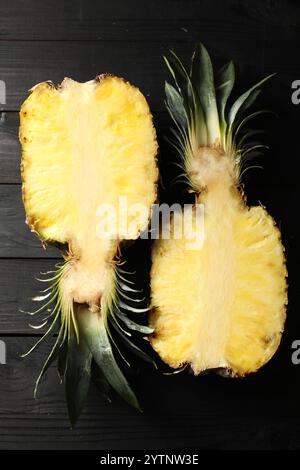 Hälften reifer Ananas auf schwarzem Holztisch, Draufsicht Stockfoto