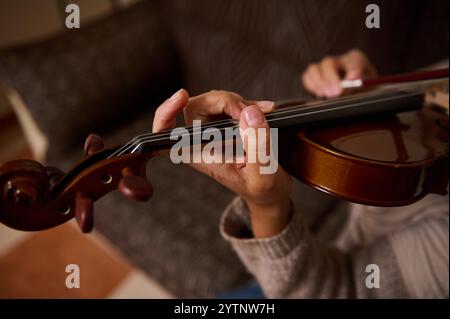 Detaillierte Ansicht der Hände eines Musikers, der auf der Geige spielt, und hebt das Können und die Konzentration in einer intimen Innenumgebung hervor. Stockfoto