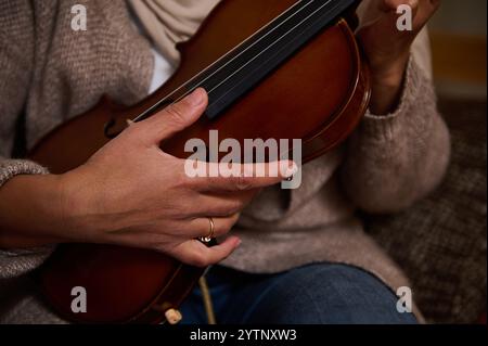 Ein detaillierter Blick auf die Hände, die sanft eine Geige halten, und die feine Handwerkskunst in einer gemütlichen Umgebung demonstrieren. Stockfoto