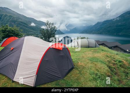 Zelte auf grünem Hügel mit Blick auf einen ruhigen Fjord mit nebeligen Bergen im Hintergrund. Malerischer Campingplatz unter bewölktem Himmel, der die Ruhe von na einfängt Stockfoto