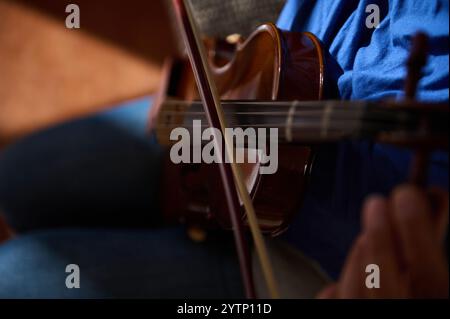 Detaillierte Ansicht eines Geigers, der ein Holzinstrument spielt, wobei Streicher und Bogendetails hervorgehoben werden. Stockfoto