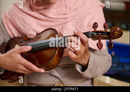 Ein detaillierter Blick auf eine Person, die geschickt eine Geige spielt und ihre Hände und das Instrument in einer gemütlichen Umgebung betont. Stockfoto