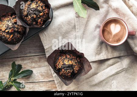 Schokoladenmuffins auf einer Serviette auf Holzbrett und Kaffeetasse, Blick von oben. Rustikales Stillleben. Farbe des Jahres 2025 - Mocha Mousse. Stockfoto