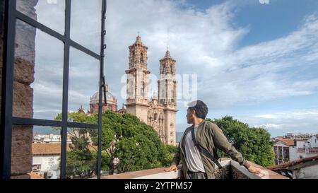 Ein Reisender steht mit Blick auf die malerische Landschaft von Taxco de Alarcon, Guerrero. Die markanten Doppeltürme einer historischen Kirche erheben sich majestätisch Stockfoto