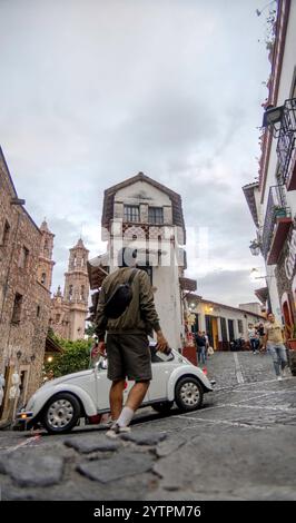 In der bezaubernden Stadt Taxco de Alarcon schlendert eine Person entlang einer kopfsteingepflasterten Straße, umgeben von historischen Gebäuden und lebendiger Kultur. Stockfoto