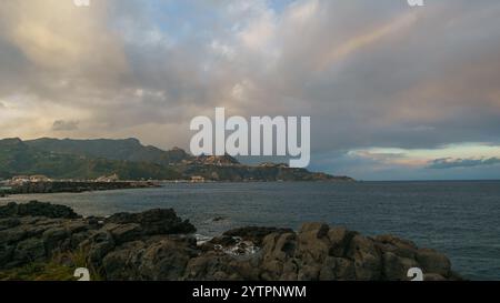 Blick auf die Bucht von Giardini Naxos zum Kap Taormina an einem bewölkten Frühlingsabend bei Sonnenuntergang, Naxos, Sizilien, Italien Stockfoto