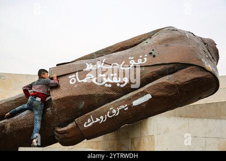 7. Dezember 2024: Hama, Syrien. Dezember 2024. Die abgerissene Statue des ehemaligen syrischen Präsidenten Hafez al-Assad in der syrischen Stadt Hama nach dem Vormarsch syrischer Rebellengruppen unter der Führung von Hayat Tahrir al-Sham. Eine große Anzahl von Kindern posierte in der Nähe der Statue, während sich die Ereignisse schnell entfalten, während der rasche Vormarsch der Opposition in Syrien, der am 27. November begann (Foto: © Juma Mohammad/IMAGESLIVE via ZUMA Press Wire) NUR REDAKTIONELLE VERWENDUNG! Nicht für kommerzielle ZWECKE! Stockfoto