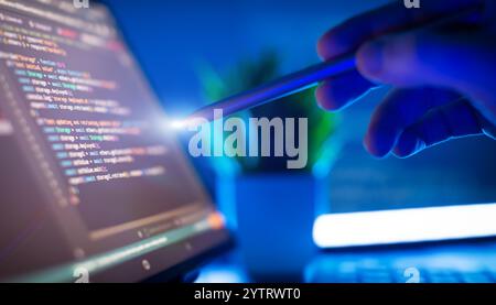 Hand mit Stylus, die mit Code auf einem Laptop-Bildschirm interagiert und Software-Entwicklung, Programmierung, Stockfoto