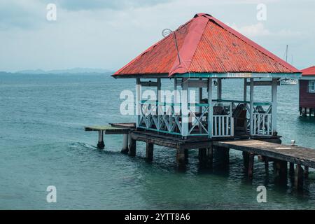 Cottages oder Holzhäuser auf dem Wasser in Bocas del Toro, mit sichtbarem, ruhigem, blauem Wasser, rotem Blechdach und blauen Holzpfählen. Stockfoto