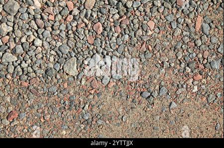 Steinoberfläche, Hintergrund. Detaillierte Textur der Straße, die mit Granitsteinen übersät ist. Chaotische Steinkulisse. Straßenfundament mit Steinen Stockfoto