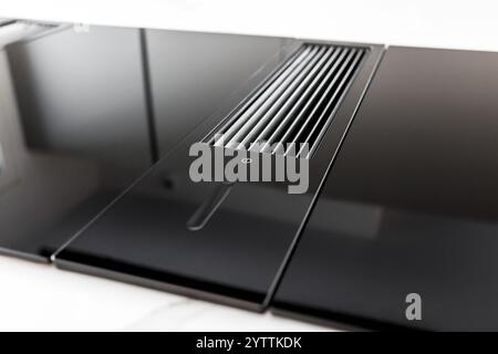Großansicht von Induktionskochfeld aus schwarzem Glas mit integrierter Abzugshaube oder Ansaugkochfeld auf heller Marmorplatte aus Steinzeug auf Küchenschrank. Stockfoto