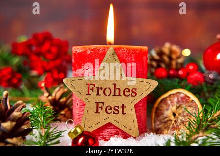 Bayern, Deutschland - 11. November 2024: Eine brennende rote Kerze, verziert mit einem Stern mit der Inschrift: Frohe Weihnachten. Umgeben von Weihnachtsdekorationen wie Tannenzweigen *** eine brennende rote Kerze, verziert mit einem Stern mit der Aufschrift: Frohes fest. Umgeben von weihnachtlicher Dekoration wie Tannenzweigen Stockfoto