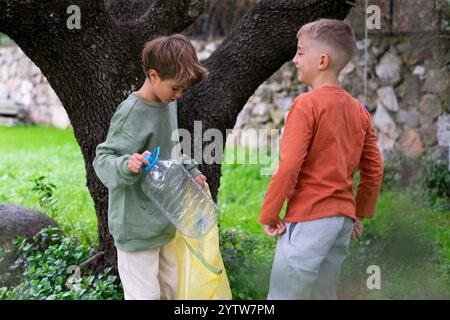 Zwei kleine Jungen stecken eine Plastikflasche in einen gelben Müllsack, um das Umweltbewusstsein zu fördern Stockfoto