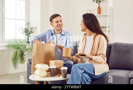 Glückliche Familie genießt Mittagspause zu Hause und bestellt Essen zum Mitnehmen, lächelndes Paar lacht beim Essen von Fast Food Stockfoto