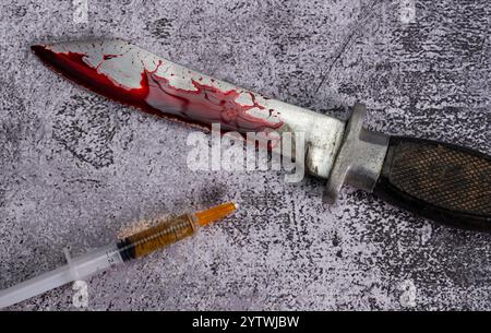 Ein Kampfmesser in Blut liegt neben einer Spritze auf einem Marmorhintergrund. Hochwertige Fotos Stockfoto