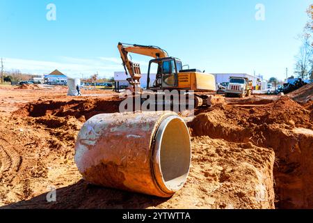 Schwere Baggermaschinen werden auf der Baustelle während der Erdbewegung eingesetzt, während die Arbeiter mit Ausrüstungsmaterialien umgehen Stockfoto