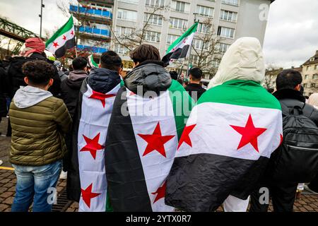 08. Dezember 2024, Nordrhein-Westfalen, Wuppertal: Teilnehmer einer Kundgebung mit syrischer Flagge als Mantel. Foto: Christoph Reichwein/dpa Stockfoto