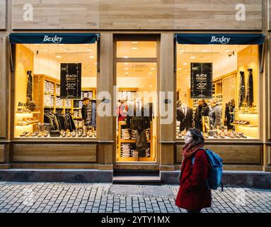 Straßburg, Frankreich - 29. November 2024: Elegantes Geschäft in Bexley, das Schuhe und Anzüge präsentiert, beleuchtet während eines Black Friday-Verkaufs, mit einem Fußgänger, der vorbeifährt Stockfoto