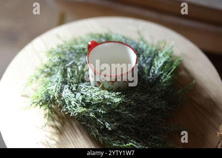 Gemütliche Winterstimmung mit einer weißen Tasse und festlichem Grün für eine Urlaubsatmosphäre Stockfoto