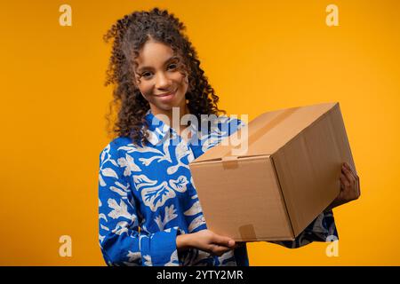 Aufgeregt lächelndes afroamerikanisches Teenager-Mädchen, Online-Shopping-Verbraucher erhielt Pappkarton, gewünschten Kauf. Zustellung per Kurierdienst Stockfoto