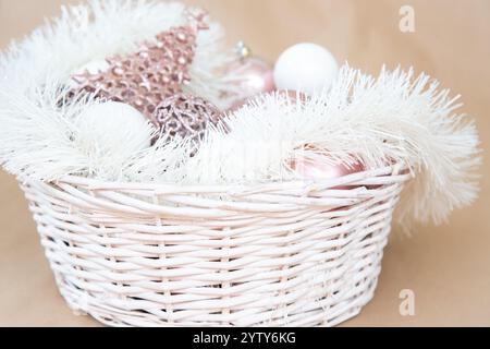 Ein wunderschön gestalteter weißer Korb, der mit einer reizvollen Auswahl an rosa und weißen Weihnachtsdekorationen überflutet wird Stockfoto