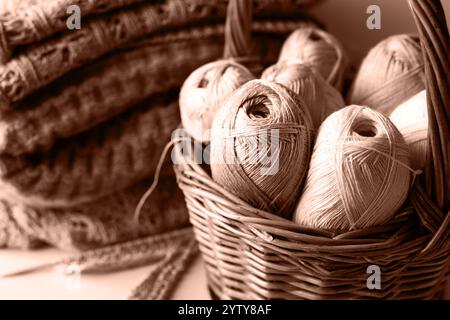 Garnfäden im Korb zum Stricken von warmer Kleidung mit Stricknadeln und fertigen Garnprodukten, Strickhobbyarbeit. Demonstration der Farben von 2025 - Mocha Mousse. Stockfoto