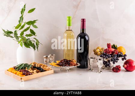 Getrocknete Früchte, frisches Obst, Nüsse, zwei Flaschen Rot- und Weißwein, silberne Gläser auf die Marmorplatte gegossen. Das Konzept des Tu BI shvat Stockfoto