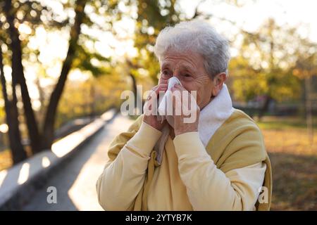 Ältere Frau mit Gewebe, das eine laufende Nase im Park bläst Stockfoto