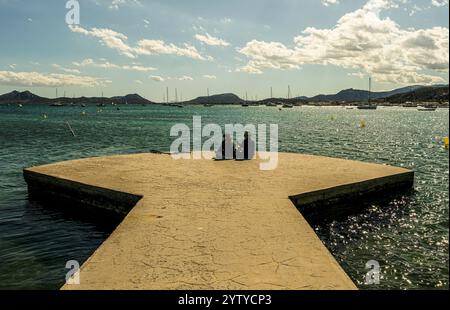 Sitzendes Paar auf dem Bootssteg mit Blick auf die Bucht von Port de Pollenca, Mallorca, Spanien Stockfoto