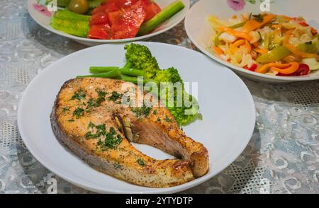 Im Ofen gebackener norwegischer Atlantischer Lachs. Lachs mit Kräutern und gekochtem Gemüse auf einem weißen Teller mit Salat und Sauerkohl. Stockfoto