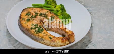 Im Ofen gebackener norwegischer Atlantischer Lachs. Lachs mit Kräutern und gekochtem Gemüse auf einem weißen Teller mit Salat und Sauerkohl. Stockfoto