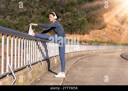 Sportliche Frau, die eine Bein-Dehnübung gegen ein Geländer im Freien macht Stockfoto
