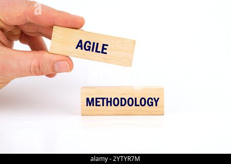Eine Hand hebt einen Block mit der Bezeichnung Agile an, während ein weiterer Block auf der Oberfläche mit der Bezeichnung Methodologie verbleibt und die Schlüsselkonzepte im Projektmanagement und symbolisiert Stockfoto