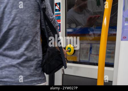Ein Mann steht vor einer Bustür und hält einen gelben Knopf. Der Mann trägt ein graues Hemd und einen schwarzen Rucksack Stockfoto