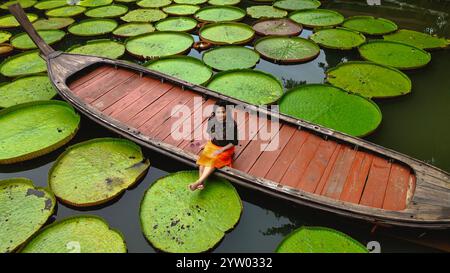 Mädchen, das auf einem Langboot sitzt, umgeben von Queen Victoria Seerosen in Phuket Thailand Stockfoto