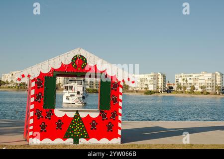 Breiter gerahmter Blick durch einen rot-weißen und grünen Weihnachtsfotostand. Großes weißes Boot im Rahmen mit Boca Ciega Bay hinten. Am St Pete Beach, F Stockfoto