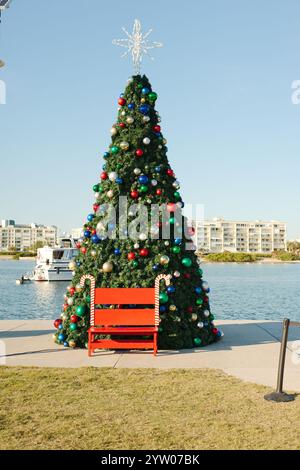 Vertikaler Blick auf einen rot, weiß und grün dekorierten Weihnachtsbaum mit Kugeln. Roter Sitz vorne mit Zuckerstangen an der Seite. Großes weißes Boot im Rahmen mit Stockfoto