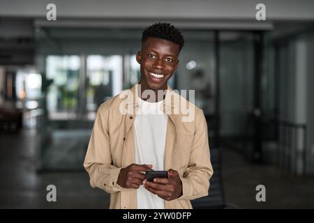 Porträt eines glücklichen afrikanischen Geschäftsmannes, der ein Smartphone benutzt, das bei der Arbeit steht. Stockfoto