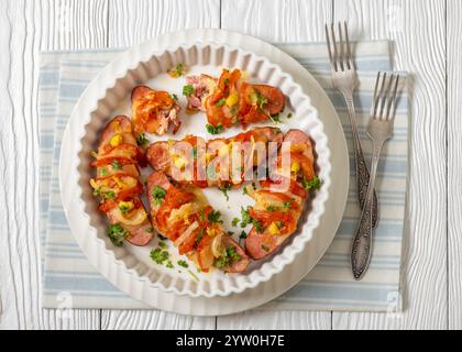 Uunimakkara, gebacken im Ofen Würstchen mit Käse, Tomaten, Senf in Backform auf weißem Holztisch mit Gabeln, finnisches Retro-Rezept, Horizont Stockfoto